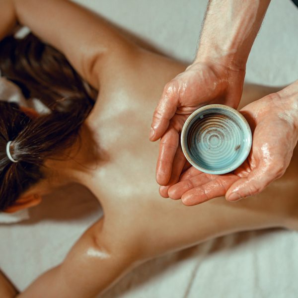 Masseur man holding bowl with warm herb infused oil for back massage Masseur man holding bowl with warm herb infused oil for back massage. Woman receiving massage at spa